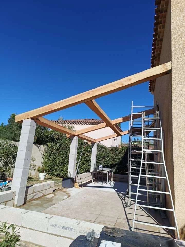 Création d'une terrasse couverte avec piliers en parpaings et charpente bois, alliant solidité et esthétique pour un espace de vie extérieur agréable.